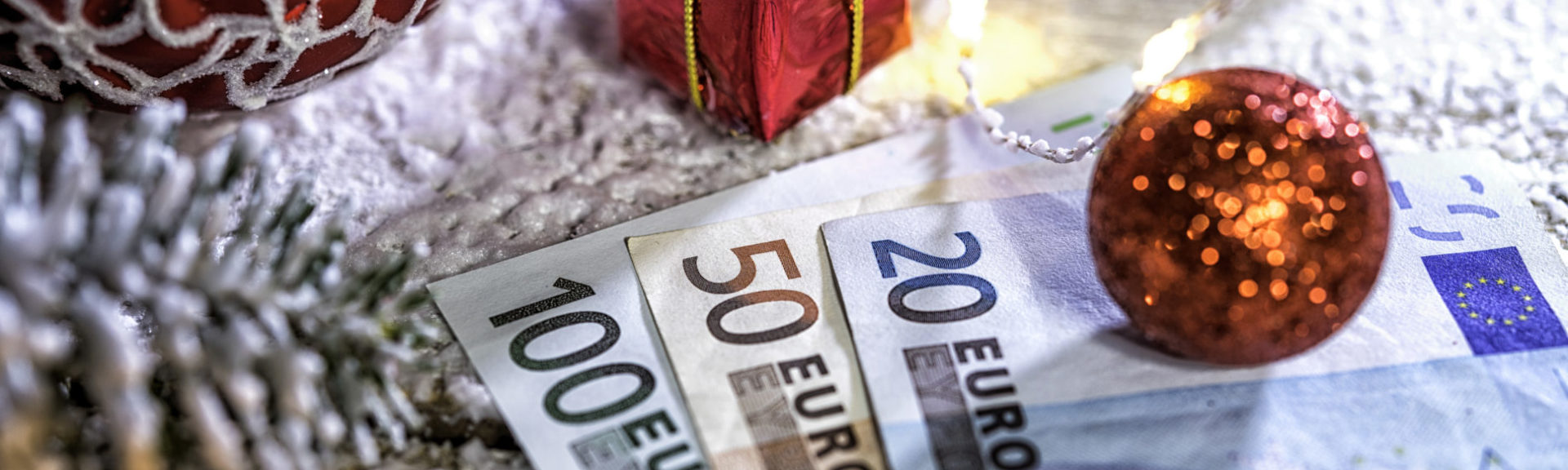 Christmas ball on old wooden table with candle and Euro banknotes