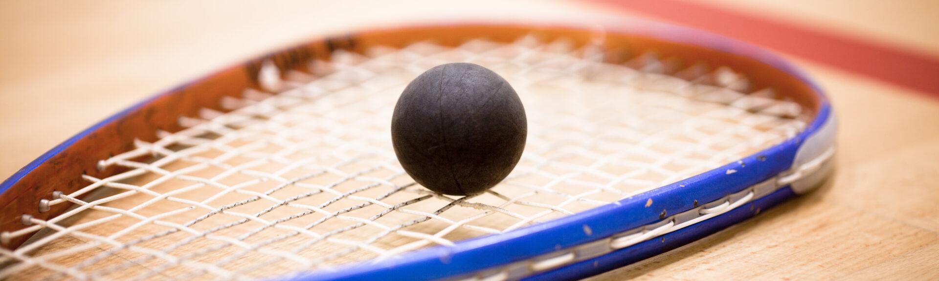 Close up of a squash ball on racket over wooden background