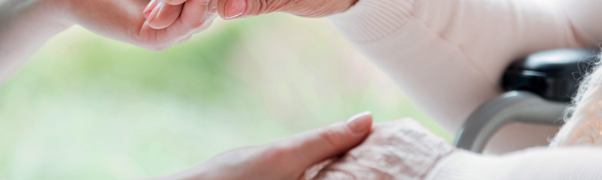 Close-up of a young woman and a senior lady holding hands with tenderness and care. Showing support and love. Blurred background.