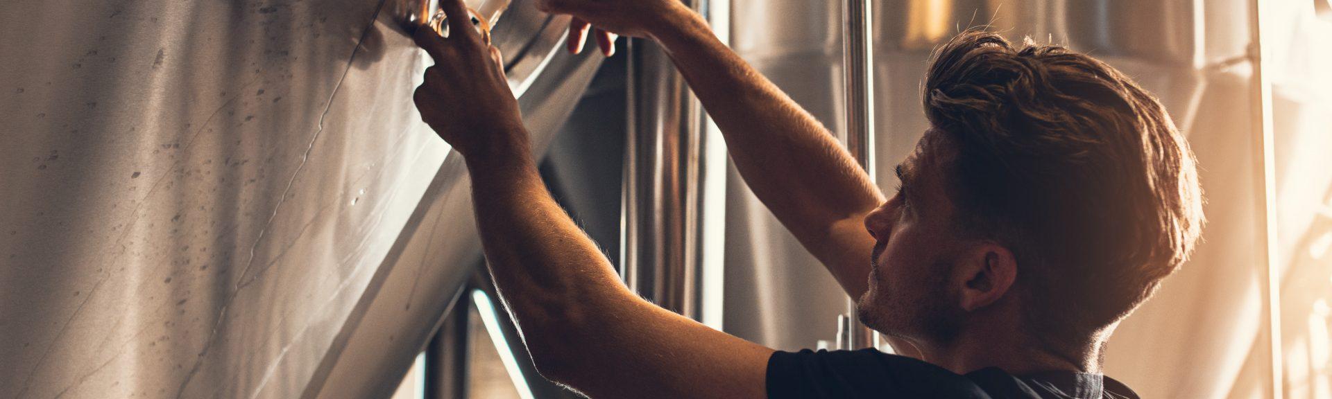 Brewer closing the hatch of brewery tank. Young male employee working in beer manufacturing factory.