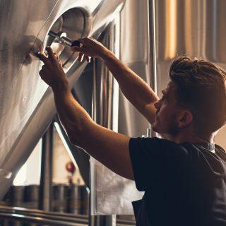 Brewer closing the hatch of brewery tank. Young male employee working in beer manufacturing factory.