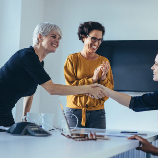 Businesswomen shaking hands and smiling during a business meeting with team clapping hands. Team congratulating and appreciating the performance of a colleague in meeting room.