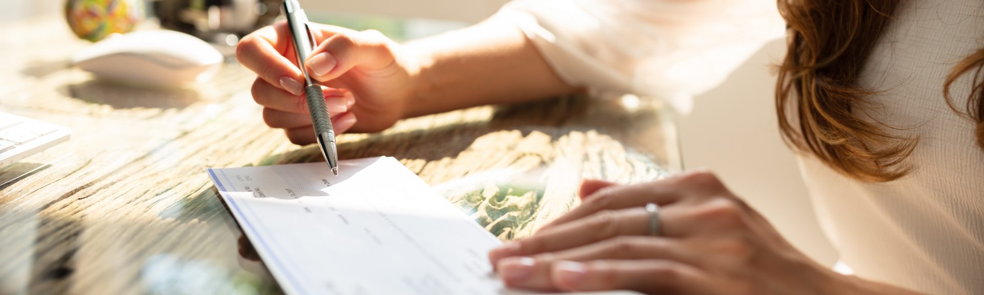 Businesswoman's Hand Signing Cheque On Wooden Desk
