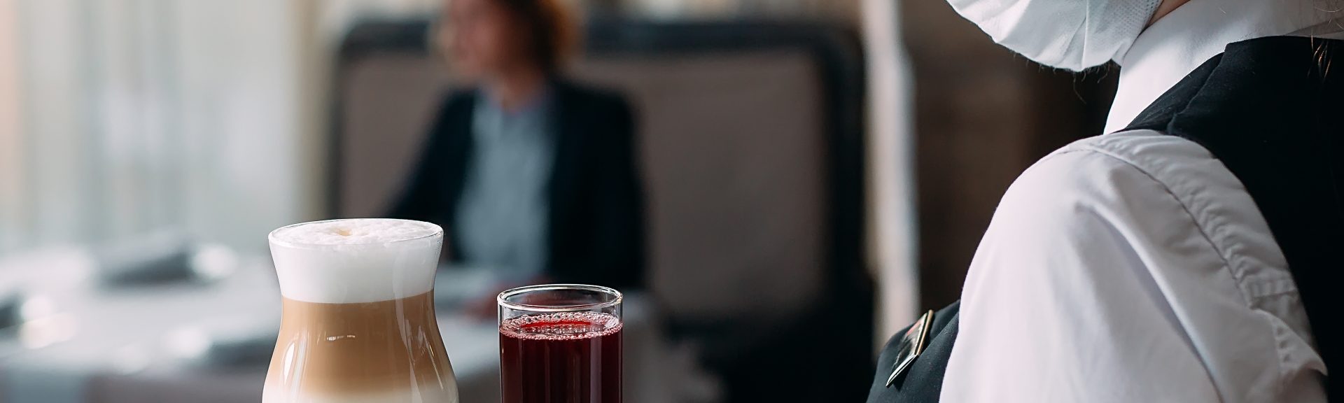 A female Waiter of European appearance in a medical mask serves Latte coffee