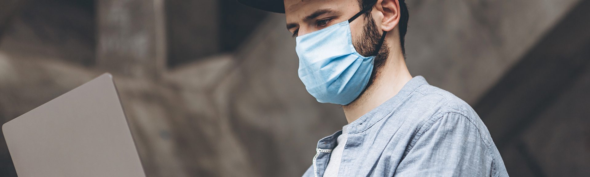 Man wearing mask and casual wear with laptop in his hands working remotely on the outside