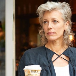 Woman with grey hair comes out of a coffeeshop