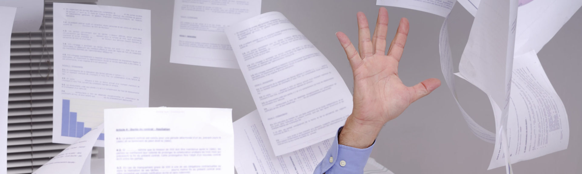Hand of business man sticking out of a desk full of papers and flying papers