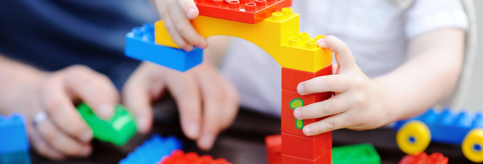 Father with his toddler son playing with colorful plastic blocks. Family leisure with little kids