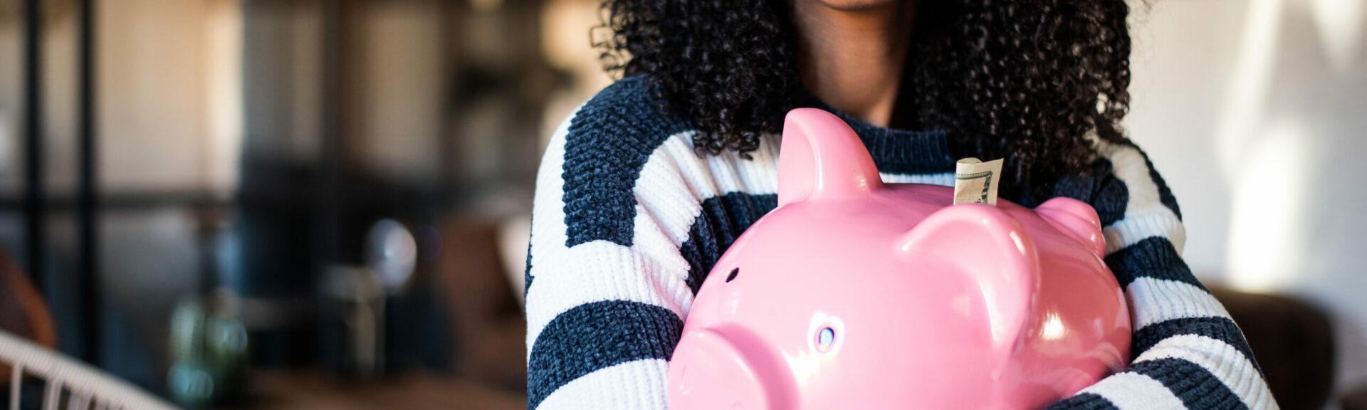 Black young woman hugging her pink piggy bank