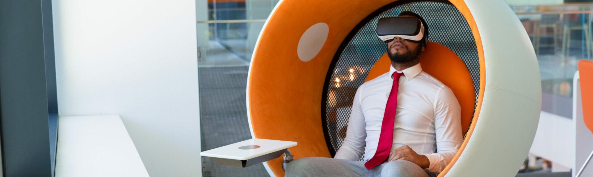 Peaceful businessman in VR headset enjoying virtual video. Man in office clothes and virtual reality goggles sitting in interactive chair and relaxing. Virtual content watching concept