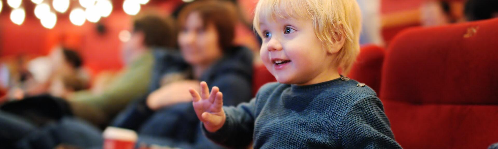 Cute toddler boy watching cartoon movie in the cinema. Leisure/entertainment for family with kids.