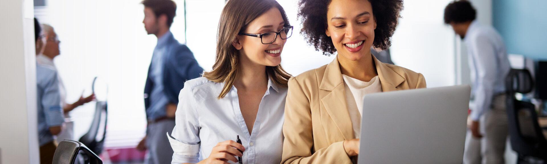 Happy multiethnic success business women working together online on a laptop in corporate office.