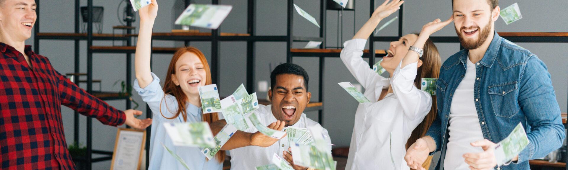 Cheerful business team of young multi-ethnic employees celebrating victory and big profit at office workplace. Cheerful excited young business man and woman throwing away banknote. Rain of money.