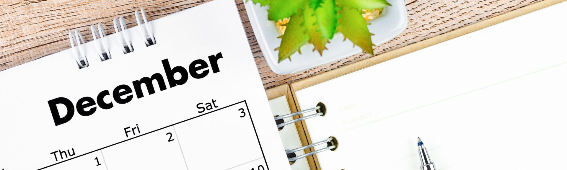 The December 2022 desk calendar and open diary with pen on wooden background.