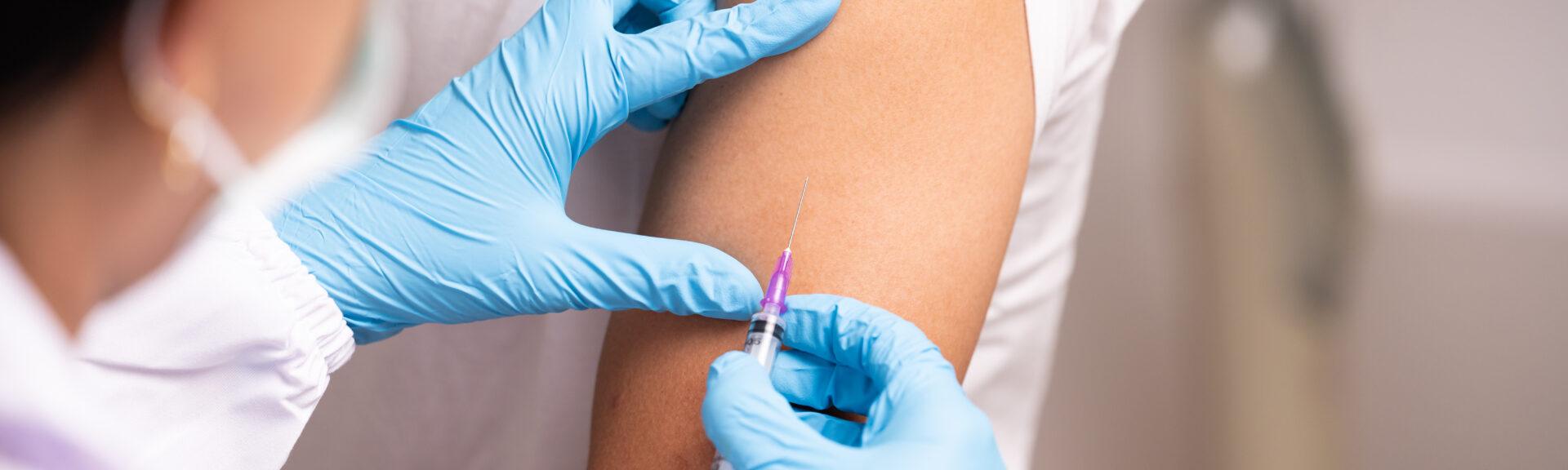 Doctor hand in blue gloves holding influenza vaccine for prevention human.Nurse holding syringe make injection in shoulder of patient in hospital.Covid-19 or coronavirus vaccine.
