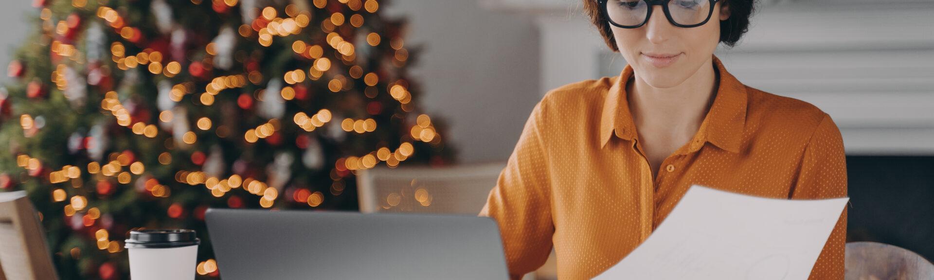 Female entrepreneur working online on laptop at Christmas in office with xmas tree in background