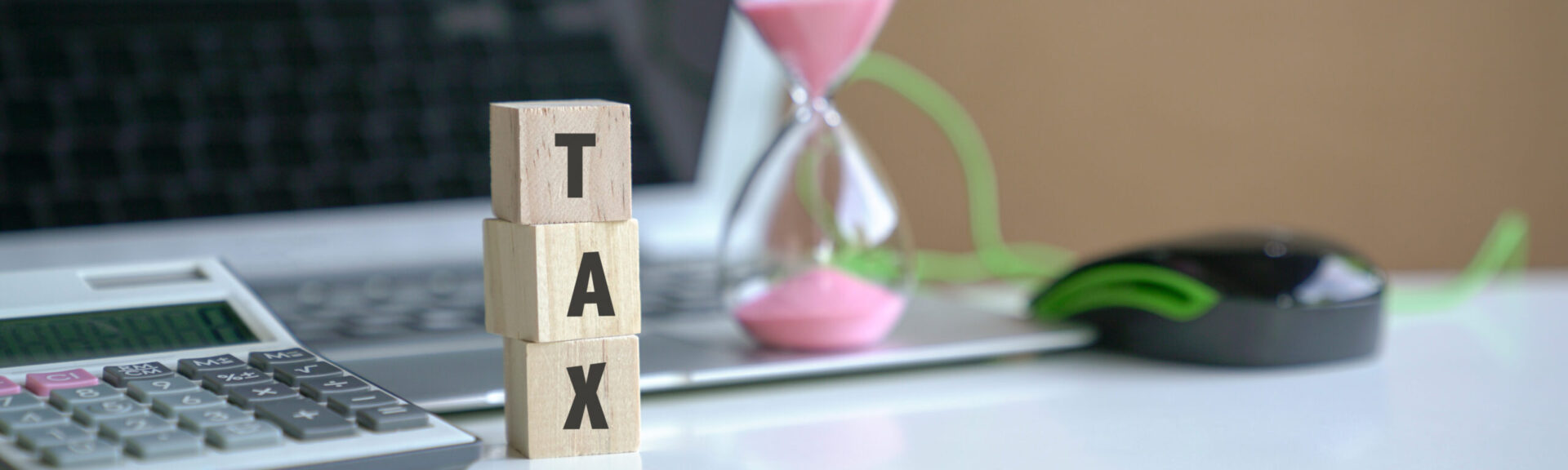 The word Tax on wooden cubes, next to computer laptop, calculator and sand timer. Tax filing concept.