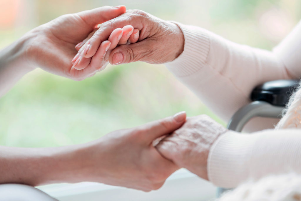 Close-up of a young woman and a senior lady holding hands with 